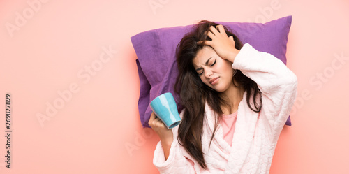 teenager girl in dressing gown over pink backgrounnd and stressed and holding a cup of coffee