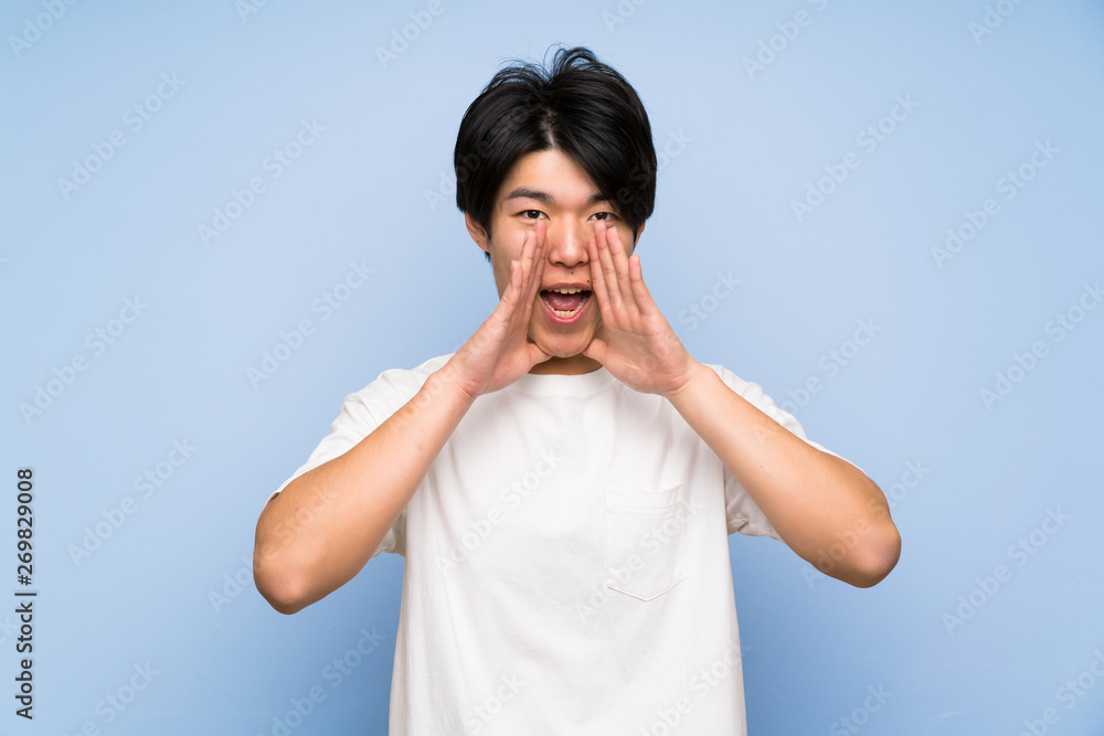 Asian man on isolated blue background shouting with mouth wide open Asian man on isolated blue background shouting with mouth wide open