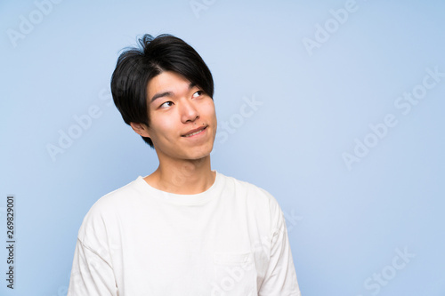 Asian man on isolated blue background laughing and looking up