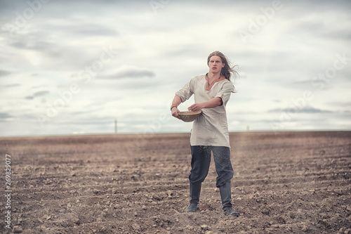 Fotografija A young peasant sows the field with grain
