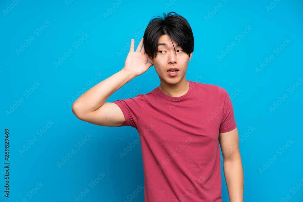 Asian man with red shirt over isolated blue wall listening something Asian man with red shirt over isolated blue wall listening something