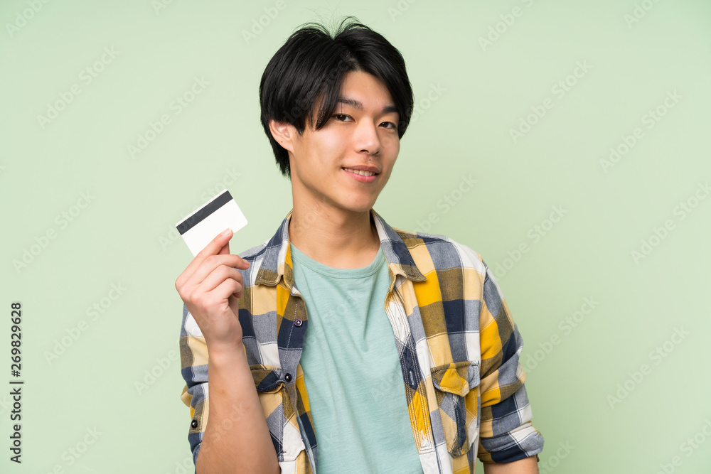 Asian man over isolated green wall holding a credit card Asian man over isolated green wall holding a credit card