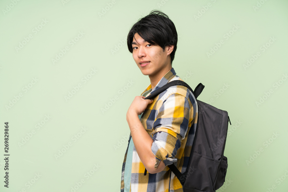 Asian man over isolated green wall with backpack Asian man over isolated green wall with backpack