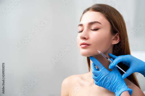 Smile lifting and lip augmentation. Beautician doctor hands doing beauty procedure to female face with syringe. Young woman's mouth countouring with filler injection. Marionette lines treatment.