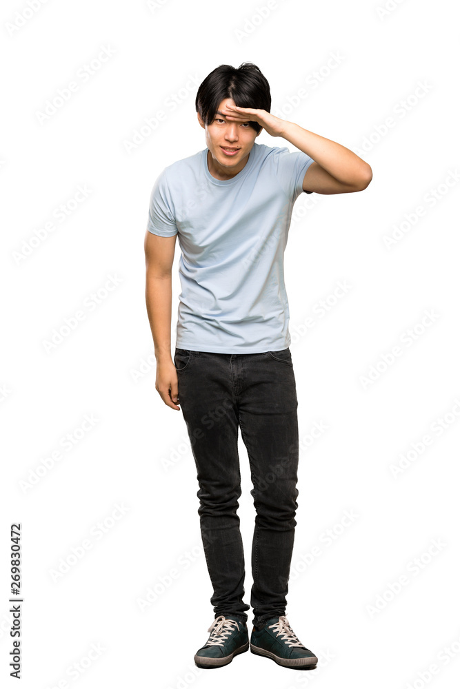 A full-length shot of a Asian man with blue shirt looking far away with hand to look something over isolated white background A full-length shot of a Asian man with blue shirt looking far away with hand to look something over isolated white background