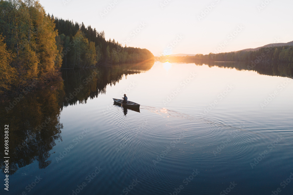 © Beatrice - Young man paddling a canoe boat towards horizon at sunset on a reflecting calm river with trees around in Europe
