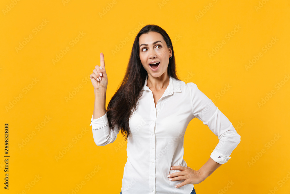 Portrait of excited young woman in white shirt holding index finger up with great new idea, looking aside isolated on yellow orange background in studio. People lifestyle concept. Mock up copy space. Portrait of excited young woman in white shirt holding index finger up with great new idea, looking aside isolated on yellow orange background in studio. People lifestyle concept. Mock up copy space.