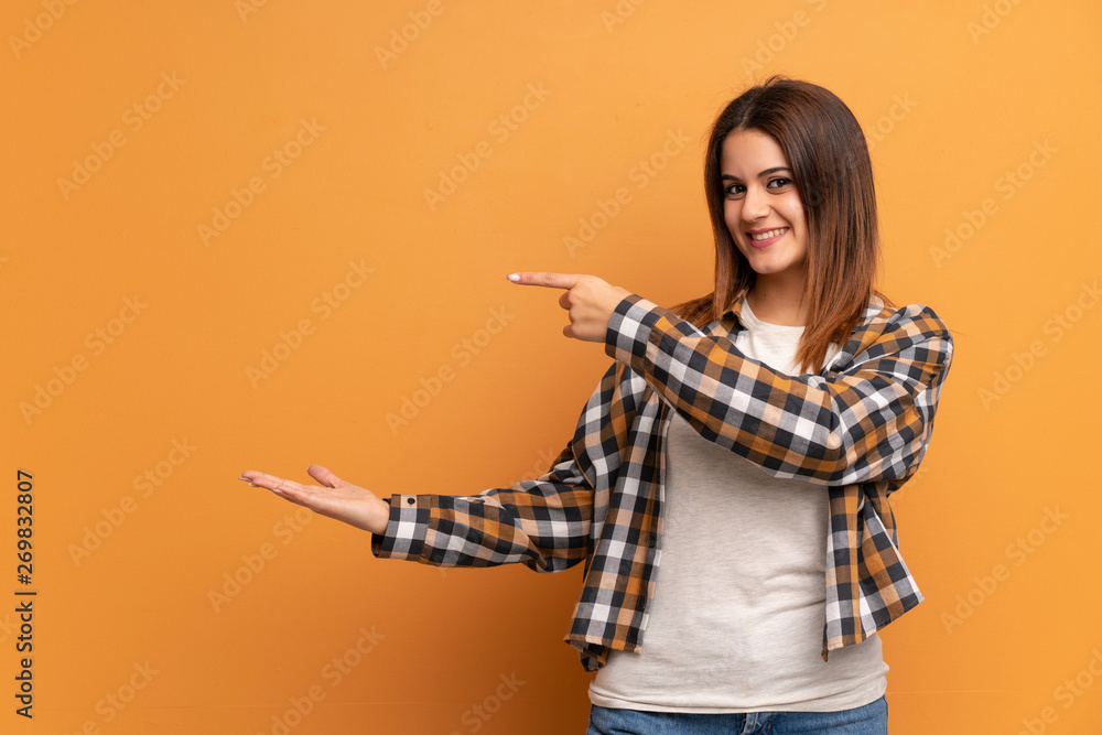 Young woman over brown wall holding copyspace imaginary on the palm to insert an ad Young woman over brown wall holding copyspace imaginary on the palm to insert an ad
