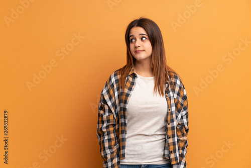 Young woman over brown wall making doubts gesture looking side