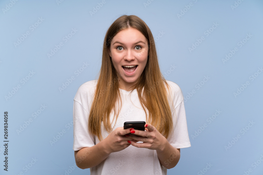 Young woman over blue wall surprised and sending a message Young woman over blue wall surprised and sending a message