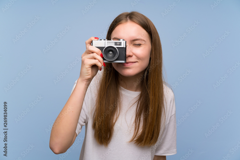 Young woman over blue wall holding a camera