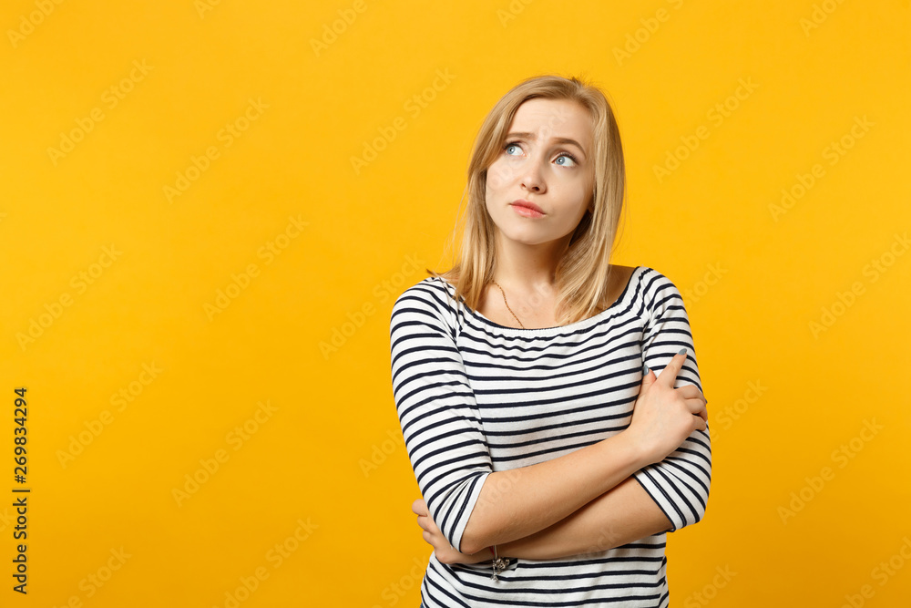 Portrait of pensive young woman in striped clothes looking aside up holding hands crossed isolated on yellow orange background in studio. People sincere emotions lifestyle concept. Mock up copy space. Portrait of pensive young woman in striped clothes looking aside up holding hands crossed isolated on yellow orange background in studio. People sincere emotions lifestyle concept. Mock up copy space.