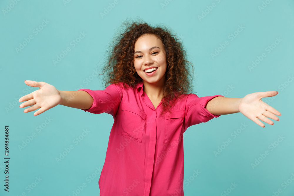 Smiling african girl in pink casual clothes standing with outstretched hands for hugs isolated on blue turquoise background in studio. People sincere emotions, lifestyle concept. Mock up copy space. Smiling african girl in pink casual clothes standing with outstretched hands for hugs isolated on blue turquoise background in studio. People sincere emotions, lifestyle concept. Mock up copy space.