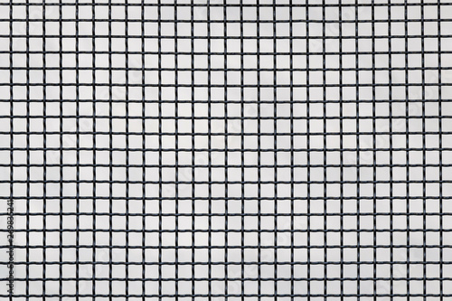 Surface of a latticed metal fence with squares elements in front of a wall made of wire; patterned weave. Metal lattice over the wall as a background texture. Selective focus. Copy space.