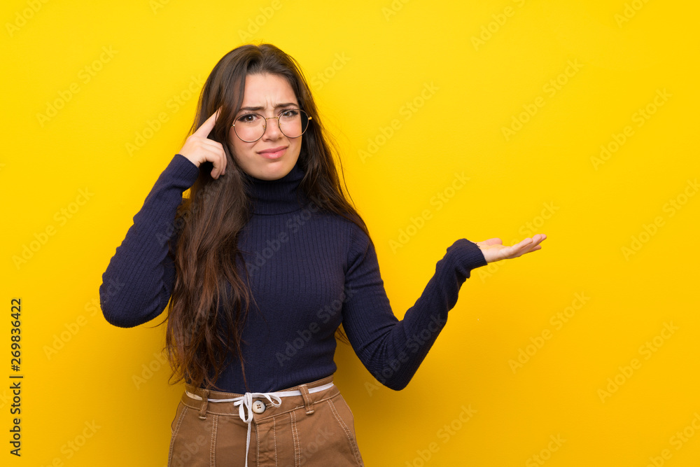 Teenager girl over isolated yellow wall making the gesture of madness putting finger on the head Teenager girl over isolated yellow wall making the gesture of madness putting finger on the head