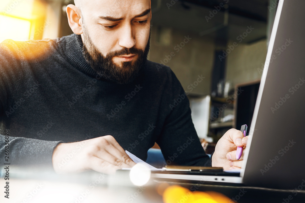 Man writes in notebook and works with computer at table in coffee shop.Freelancer works on laptop, writes in notebook in coworking Man writes in notebook and works with computer at table in coffee shop.Freelancer works on laptop, writes in notebook in coworking