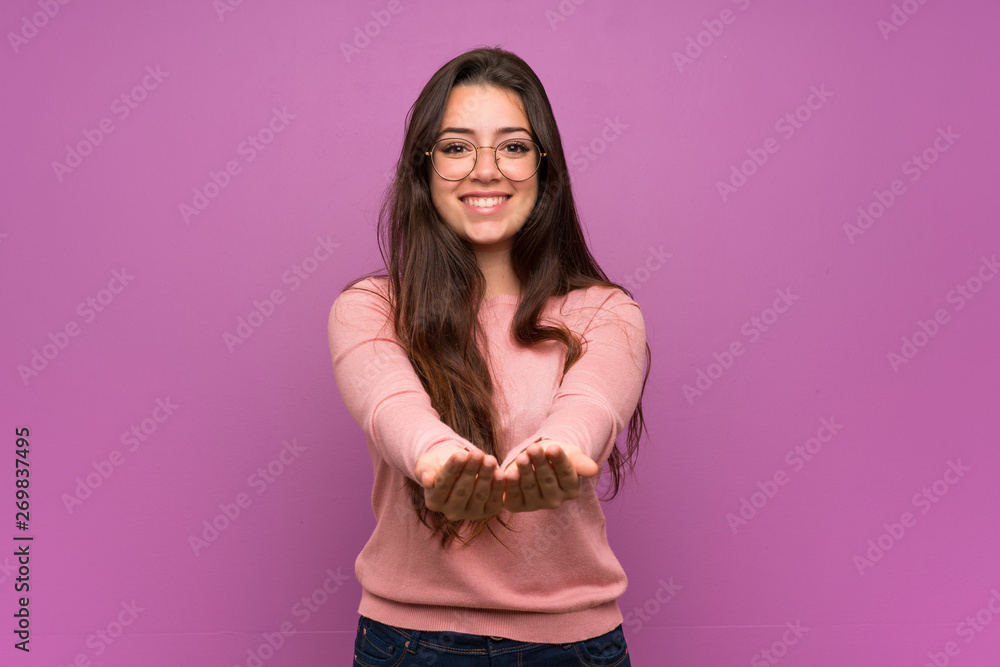Teenager girl over purple wall holding copyspace imaginary on the palm to insert an ad Teenager girl over purple wall holding copyspace imaginary on the palm to insert an ad