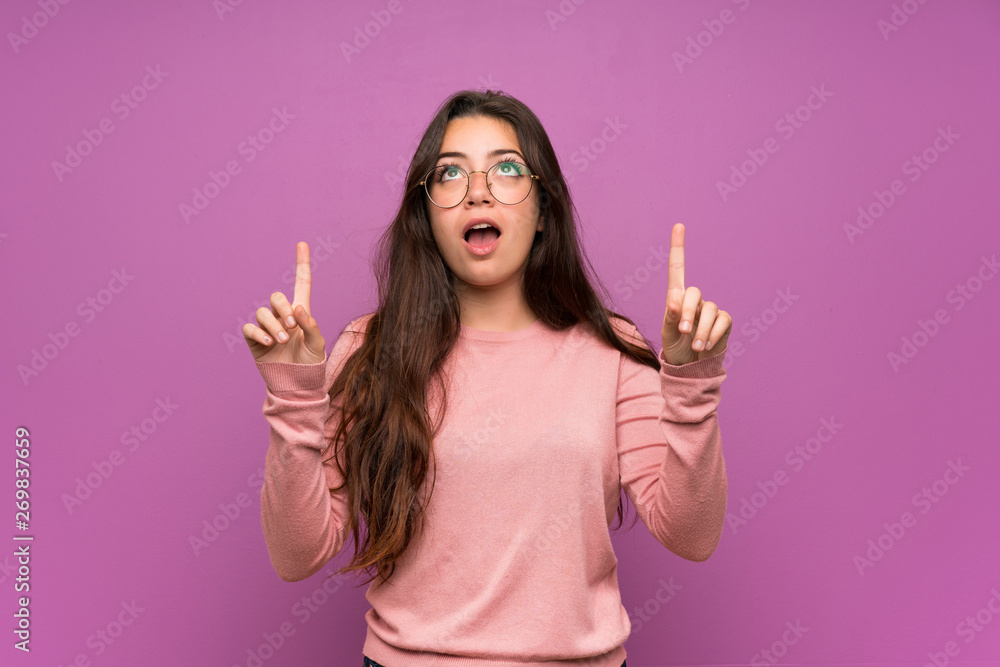 Teenager girl over purple wall surprised and pointing up Teenager girl over purple wall surprised and pointing up