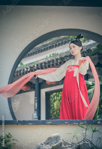 A Chinese woman dance in front of  traditional buildings in Han clothing. © imphilip