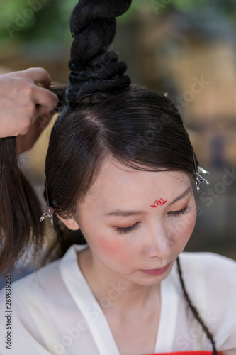 A woman is having her long hair braided before an opera show.