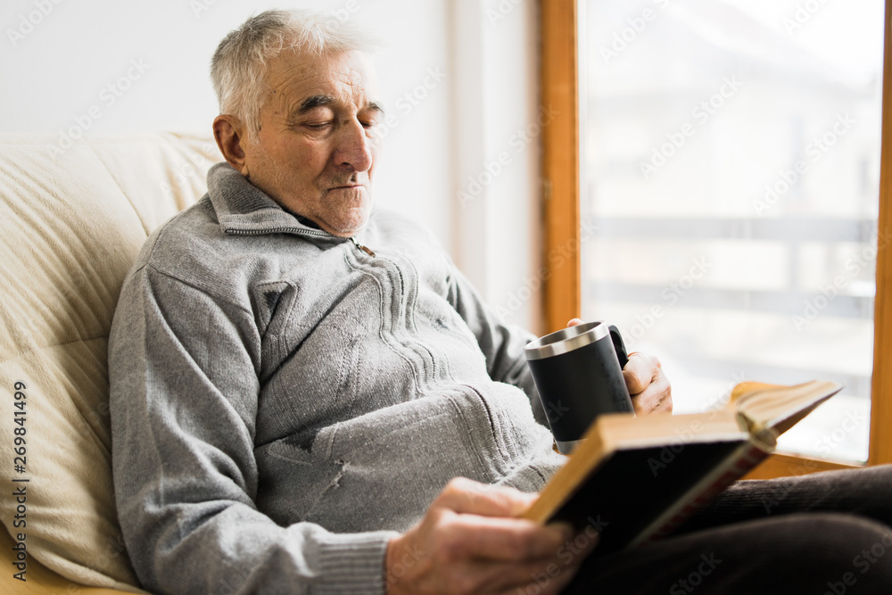 Senior man sitting and Reading a book at the retirement nursing home with cup of tea in hand Senior man sitting and Reading a book at the retirement nursing home with cup of tea in hand