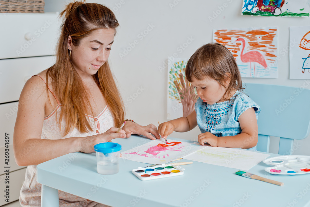 woman with a little girl holding a drawing lesson in the room at the table. woman with a little girl holding a drawing lesson in the room at the table.