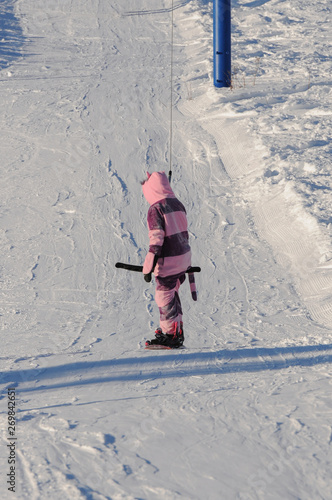A female snowboarder in a cat costume going up the slope using a T-bar lift on a sunny day photo