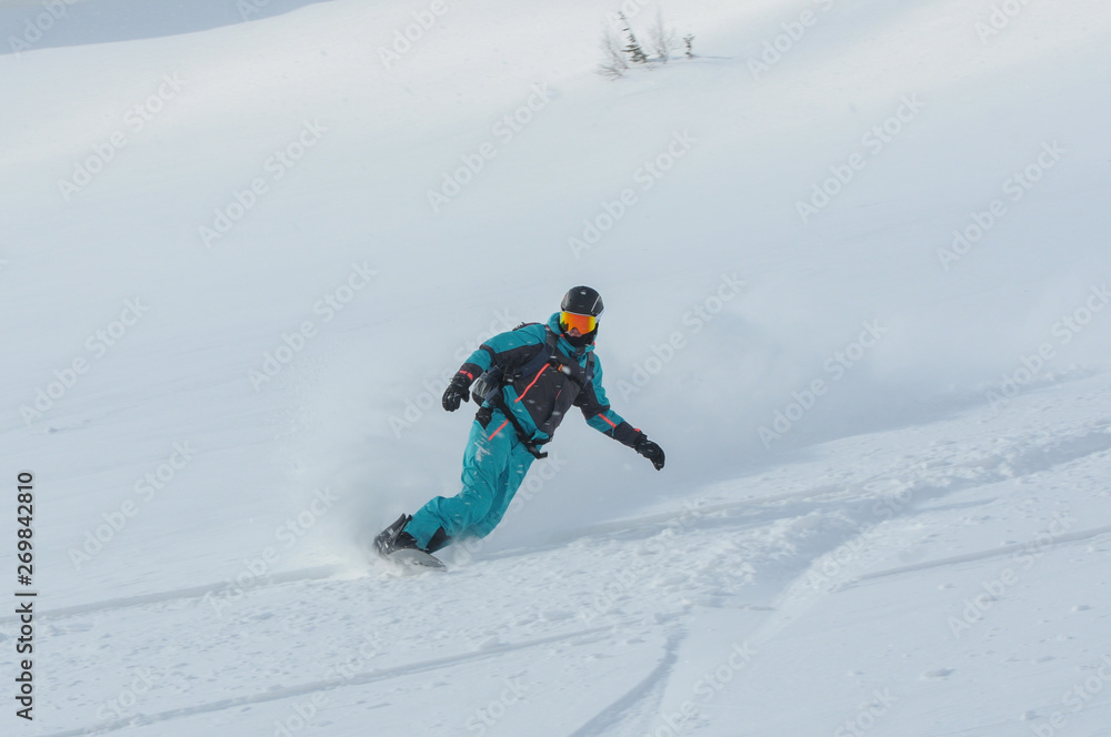 A snowboarder making a powder turn on a piste covered with fresh snow on a sunny morning A snowboarder making a powder turn on a piste covered with fresh snow on a sunny morning