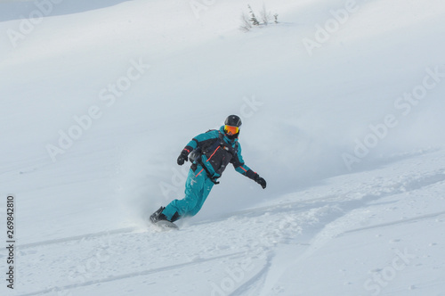 A snowboarder making a powder turn on a piste covered with fresh snow on a sunny morning