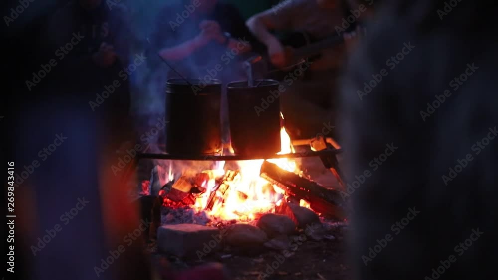 People heating up water in the buckets using a bonfire. A man playing guitar on the background People heating up water in the buckets using a bonfire. A man playing guitar on the background