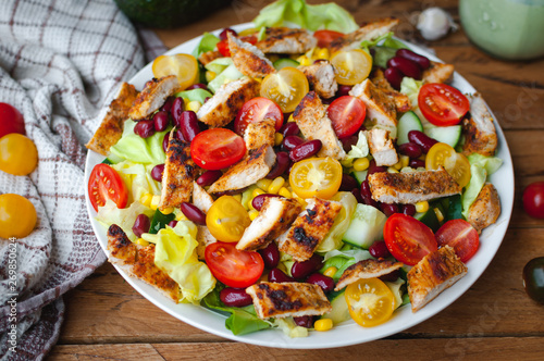 Close-up of chicken salad with fresh vegetables in a plate, on wooden background