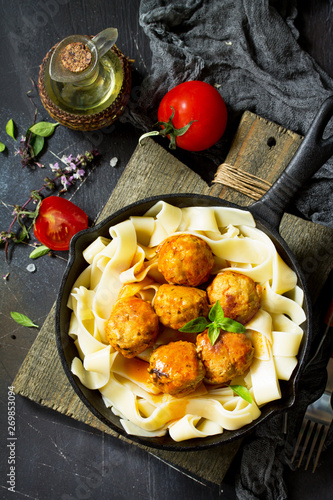 Fettuccine pasta and Homemade Beef meatballs in tomato sauce in a frying pan on dark stone table. Top view flat lay. photo