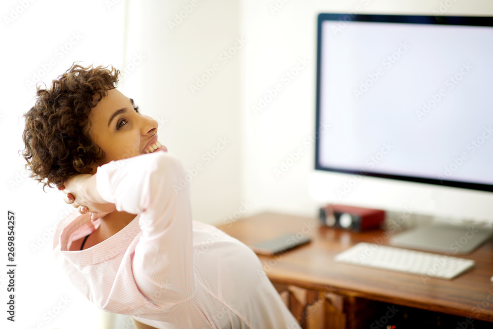 happy woman sitting by computer with hands behind head happy woman sitting by computer with hands behind head