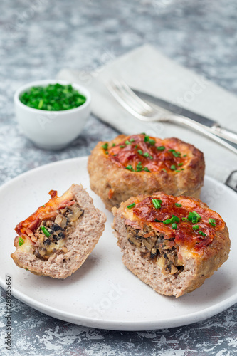 Low carb paleo meat cups, stuffed with champignons, bacon and cheese, garnished with green onion, on a white plate, vertical