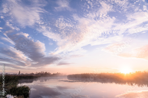 Dawn over the river on a summer morning, fog over the field, grass with hoarfrost