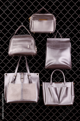 Bright fashion collection of ladies accessories. Stylish silver leather handbags on metal grid on black background. Copy Space. Mock Up.