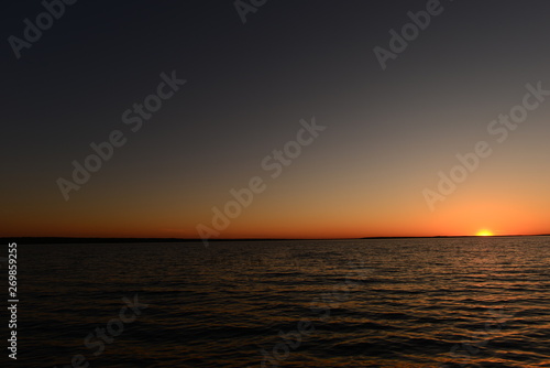 Dark sky in the glow of sunlight in a semicircle around the sun on the horizon above the water of the lake at sunset