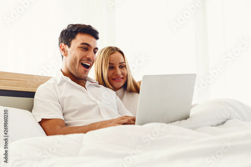 Couple caucasian lover smiling showing very happy gesture while enjoy using laptop computer together on bed early morning