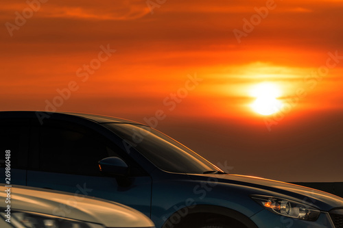 Side view of blue SUV car with sport and modern design parked on concrete road at sunset. Hybrid and electric car technology. Road trip. Automotive industry. Car parking lot with beautiful sunset. © Artinun