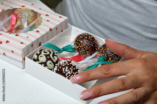 Cake pops decorated with a bow of braid, packed in a gift box. Woman closes the box.