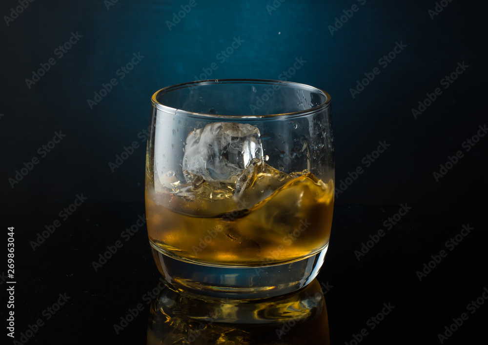 A glass of whiskey with ice on a dark color photo with splashes from falling ice A glass of whiskey with ice on a dark color photo with splashes from falling ice