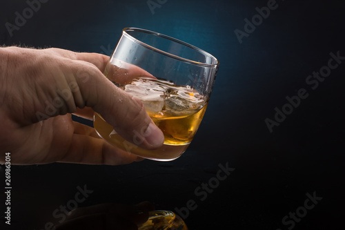A glass of whiskey with ice on a dark color photo with splashes from falling ice