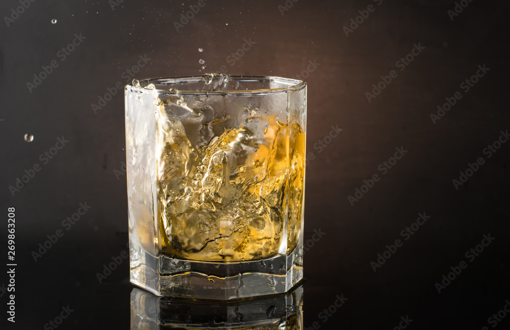 A glass of whiskey with ice on a dark color photo with splashes from falling ice A glass of whiskey with ice on a dark color photo with splashes from falling ice
