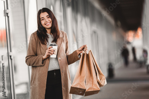 Beautiful fashionable woman with shopping bags and coffee walking near mall.