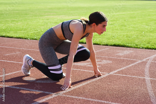 Young beautiful woman runner outdoor standing in start pose at the stadium