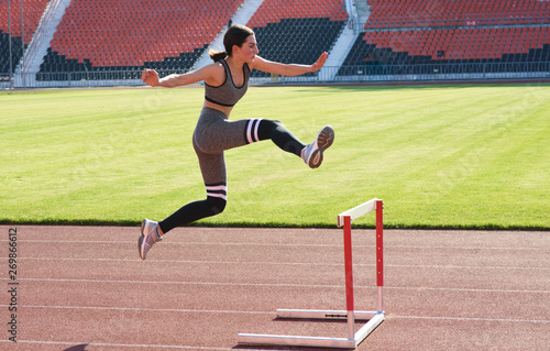 A beautiful and athletic girl is running hurdles in the stadium