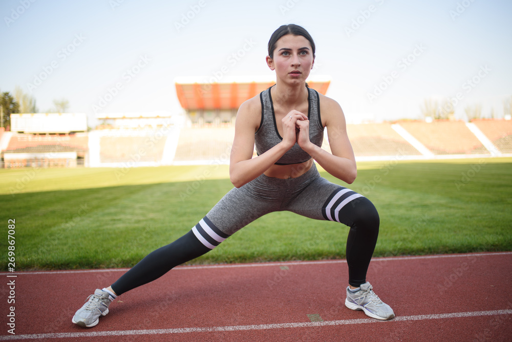 Obraz premium Beautiful athletic girl warming up before a hard workout at the stadium