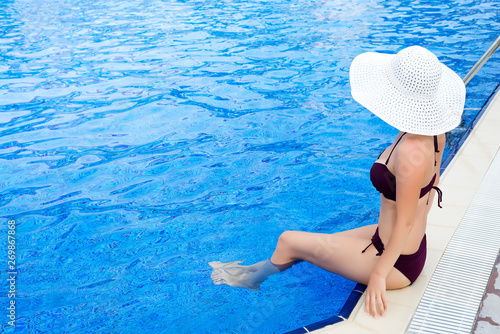 Beautiful woman in white hat and sunbathing on the pool blue water. Summer background.