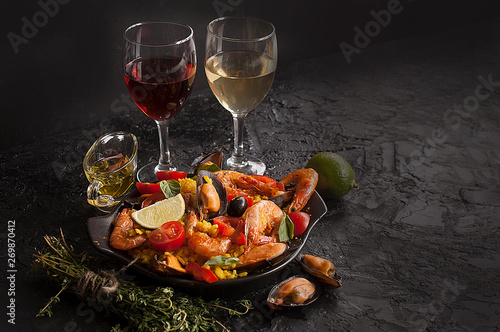 Paella on a pan with shrimp, mussels and wine on a black table. Spanish Mediterranean cuisine. Seafood is a healthy food concept. Copy space.