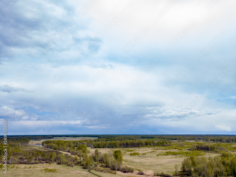 Aerial view of a landscape with green fields and forest under gray clouds and clouds on a warm spring day. Nature and the environment without people and harmful emissions. Aerial view of a landscape with green fields and forest under gray clouds and clouds on a warm spring day. Nature and the environment without people and harmful emissions.